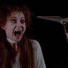 Eine Frau mit entsetztem Gesichtsausdruck sieht eine Spitzhacke, die ihr entgegengestreckt wird.