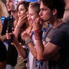 Junge Leute stehen dicht beieinander, eine Person hält ein Smartphone mit Gimbal, alle wirken aufmerksam.