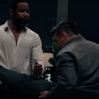 Zwei Männer kämpfen in einem dunklen Raum mit Lichtern im Hintergrund; links einer in offener weißer Bluse.