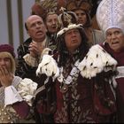 Eine Gruppe von Menschen in opulenten, historischen Kostümen drückt Überraschung und Entsetzen aus.