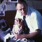 Es ist ein Mann beim Rasieren durch einen anderen. Sie befinden sich in einem Raum mit Bildern an der Wand.