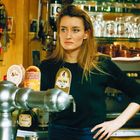 Texte: "DRINK COOL", "KINGSTON", "ADELSCOTT", "DESPERADOS", "FISCHER GOLD".  
Eine Person steht hinter einer Zapfanlage in einer Bar.