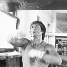 Ein Mann trainiert konzentriert an einem Speedball in einem Fitnessstudio. Er trägt ein ärmelloses Shirt.
