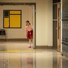 Ein Flur mit gelben Tafeln an der Wand. Ein Mädchen in rotem Kleid schaut neugierig aus einer offenen Tür.