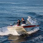 Ein Motorboot auf dem Meer. Zwei Männer sitzen fröhlich darin, während es schnell über das Wasser fährt.