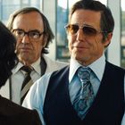 Zwei Männer, der eine trägt eine bräunliche Brille und eine bunte Krawatte. Der Hintergrund ist unscharf.