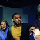 Vier Menschen in einem dunklen Raum wirken angespannt. Einer hält eine Axt, andere haben Verletzungen.