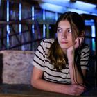 Ein Mädchen in gestreiftem Shirt stützt ihren Kopf auf die Hand, sitzt nachdenklich in einem dunklen, hölzernen Raum.