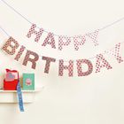 „Happy Birthday“-Girlande, Herzmuster. Roter Geschenkkarton mit Schleife, grüne Karte mit Torte, auf Regal.