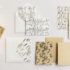 Mehrere Umschläge und Karten mit floralen Mustern in Schwarz und Gold auf hellem bis beigem Papier.