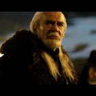 Ein älterer Mann mit langem weißem Haar und Bart, trägt einen dicken, pelzbesetzten Mantel. Er blickt ernst.