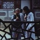 Zwei Personen in traditionellen asiatischen Gewändern stehen hinter einem kunstvoll gestalteten Holzgitter in einem Innenhof.