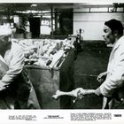 „THE GLOVE“ unten rechts. Zwei Männer in Arbeitskleidung hantieren in einer Fleischerei vor einem Behälter voller Knochen.