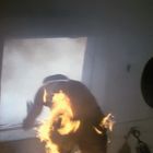 Ein Menschensilhouette springt aus einem Fenster, umgeben von Flammen. Wenig Licht und Rauch im Hintergrund.