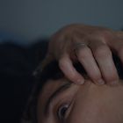 Eine Hand mit einem Ring berührt den Kopf eines Menschen, nahe dem Auge.