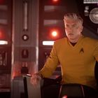 Ein Mann in gelber Uniform mit einem Abzeichen sitzt auf einem Stuhl, umgeben von technischen Elementen und roten Lichtern.
