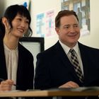 Ich kann keine Texte und Details erkennen, aber es sind zwei lächelnde Personen in Anzügen in einem Büro zu sehen.