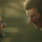 Zwei Männer stehen sich nahe gegenüber. Der eine trägt eine Brille, der andere schaut intensiv. Licht fällt auf ihr Gesicht.