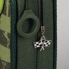 Ein grüner Stoff mit einem Reißverschluss. Ein Metallanhänger zeigt zwei gekreuzte Zielflaggen.