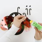 "Bastelleber" steht auf der Kleberflasche. Hände basteln an einem Marienkäfer aus Papier.