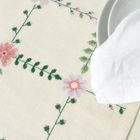 Bestickte Tischdecke mit Blumenmustern. Ein Teller mit weißer Serviette liegt darauf.