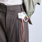 Ein flauschiger Wolkenanhänger mit Gesicht, Regenbogenperlen, an einer grauen Hose befestigt.