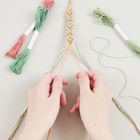 Zwei Hände knüpfen ein farbenfrohes Armband aus Garnen in verschiedenen Farben. Links und rechts liegen Garnbündel.