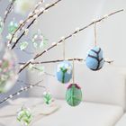 Zweige mit verzierten Eiern, darunter filzartige und glasige Designs, hängen dekorativ an einem Ast.