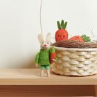 Ein Filzhase in grün hält eine Karotte. Daneben ein Korb mit Filzmöhren mit Gesichtern in einem Nest aus Zweigen.