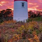 Der Oktober-Kalender zeigt einen rot-weißen Leuchtturm bei Sonnenuntergang, umgeben von herbstlicher Vegetation.