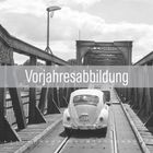 Text: "Vorjahresabbildung", "10", "2026". Ein klassischer VW Käfer fährt über eine alte, metallene Brücke in Schwarz-Weiß.