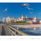 Kalenderansicht: September 2027. Ein Steg führt zu eleganten Gebäuden am Strand. Möwen fliegen am klaren Himmel.