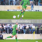 Vorjahresabbildung. Ein Fußballspieler in grüner Ausrüstung mit Ball auf dem Spielfeld. Zuschauer im Hintergrund.