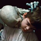 Ein Kind wird von einem skelettartigen Wesen mit fahlen Händen und einem kahlen Kopf umarmt.