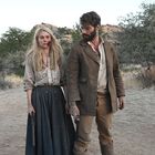 Ein Mann und eine Frau stehen in einer trockenen Landschaft mit Büschen. Beide wirken ernst, die Frau hat blutige Spuren im Gesicht.