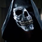 Ein Totenkopf in einer schwarzen Kapuze, beleuchtet vor dunklen Vorhängen.