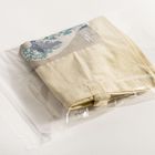 Eine beige Tasche mit einer blauen Wellengraphik liegt in einer transparenten Plastiktüte.