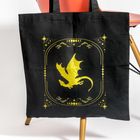 Goldener Drache umrahmt von Sternen und Mondsymbolen auf schwarzer Stofftasche, an orangem Stuhl hängend.