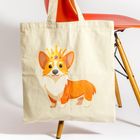 Beigefarbene Tasche mit Illustration eines Corgis mit Krone, auf einem roten Stuhl hängend.