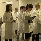 Eine Gruppe junger Menschen in weißen Laborkitteln steht dicht zusammen und macht Notizen.