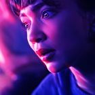 Eine Frau, beleuchtet von pinkem und blauem Licht, schaut nachdenklich zur Seite.