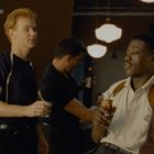 „Good for you” auf einem Guinness-Poster. Drei Männer stehen in einer Bar und trinken, zwei reden miteinander.