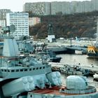 Text: "ПК-7500". im Hintergrund sind mehrere Schiffe im Hafen und ein großer Statue. Wohnhäuser und bewaldete Hügel umgeben.