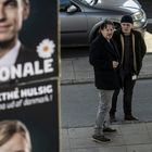 "Wörter: 'DIE NATIONALE', 'ANNE-GRETHE HULSIG'. Zwei Männer gehen auf einem Bürgersteig, Autos im Hintergrund."