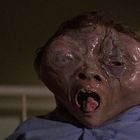 Ich kann den Text nicht erkennen. Zu sehen ist ein deformiertes, erschrockenes Gesicht in einem dunklen Raum.