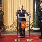 Ein rotes Wappen mit einem goldenen Adler ziert ein Podium, um das fünf Personen in Uniform versammelt sind.
