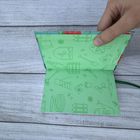 Grünes Papier mit Gartenmotiven: Spaten, Gießkanne, Blumen. Hand hält es auf Holzhintergrund.