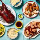 Entenbraten mit Messern, Schweinefleischstücke, Reis, Gemüse, Saucen auf blauem Tischtuch. Chinesische Mahlzeit.