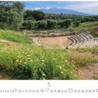 "Amphitheater" steht unten links. Ein antikes Amphitheater in einer grünen Landschaft mit Blumen und Bergen im Hintergrund.