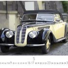 "BMW 328", darunter Kalendarium. Ein klassisches Auto mit schwarz-cremefarbenem Design auf Kopfsteinpflaster.